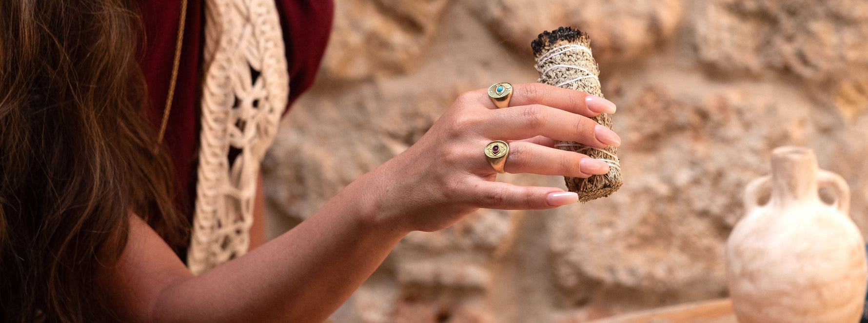 Close-up of two symbolic Eye rings in 14k gold with turquoise and ruby, worn on hand holding sage bundle – sacred Jewish jewelry