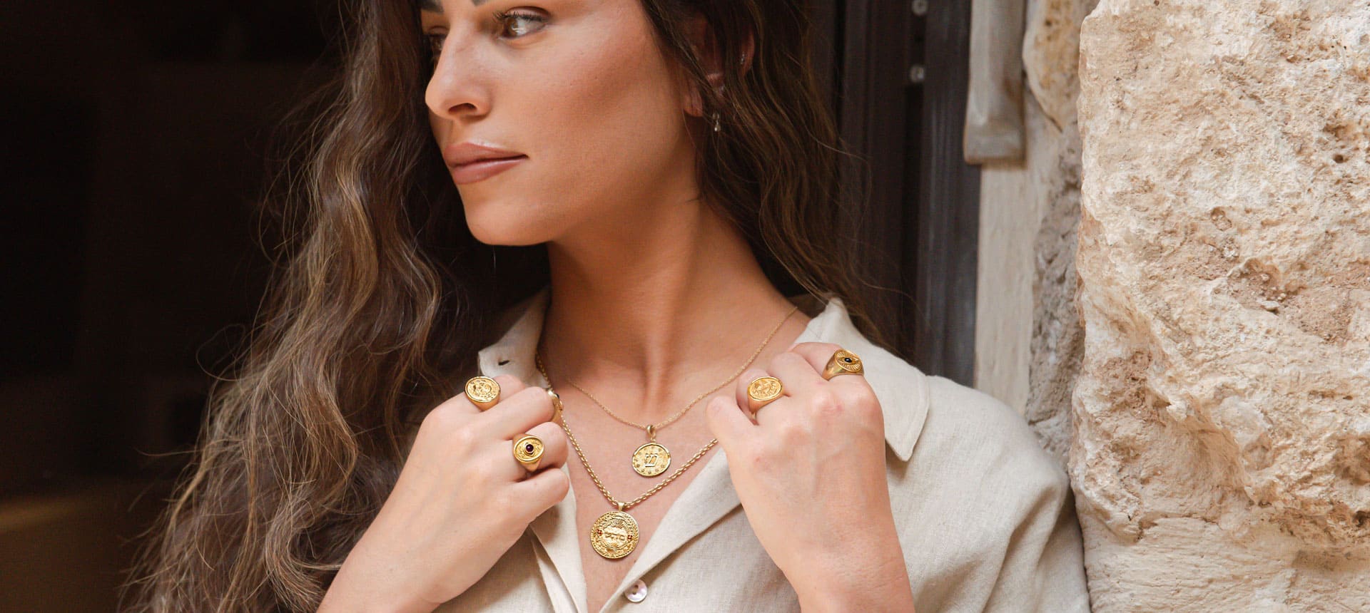 Elegant model wearing layered gold rings and pendants from the Rings Collection by Sages & Souls, photographed in a natural stone setting