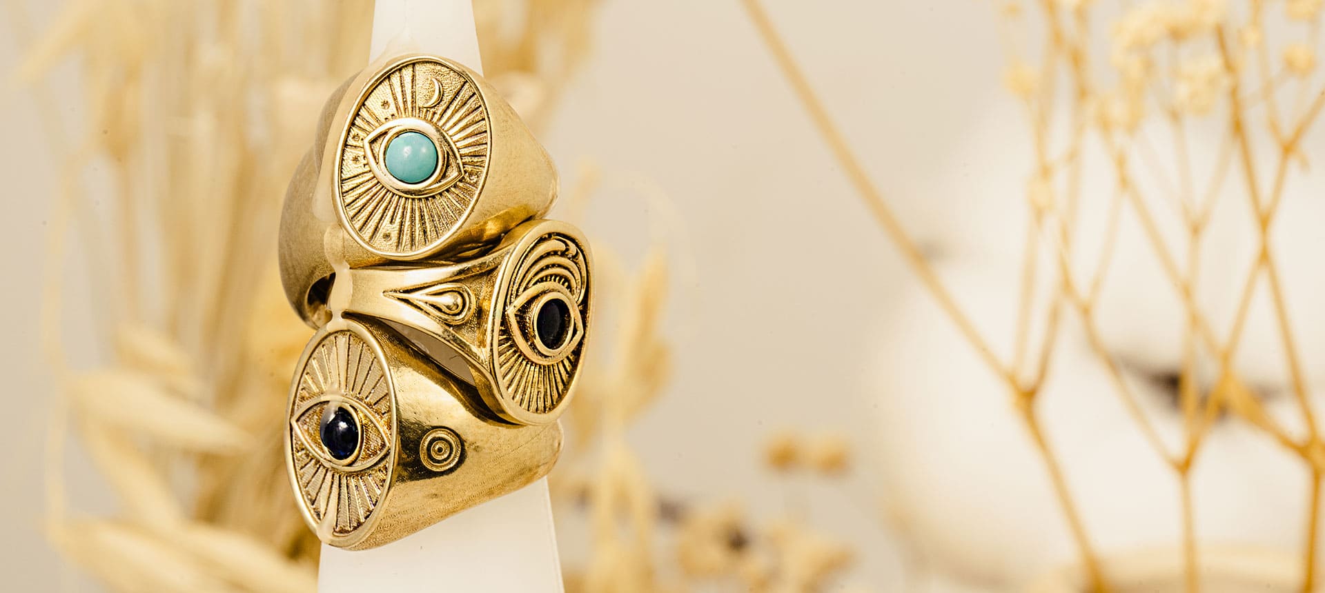 Stacked gold rings with protective eye design from the Eye Collection by Sages & Souls, styled on a white display with natural beige background