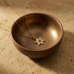 Petal Star of David necklace with pink sapphire resting inside a brass bowl on stone background.