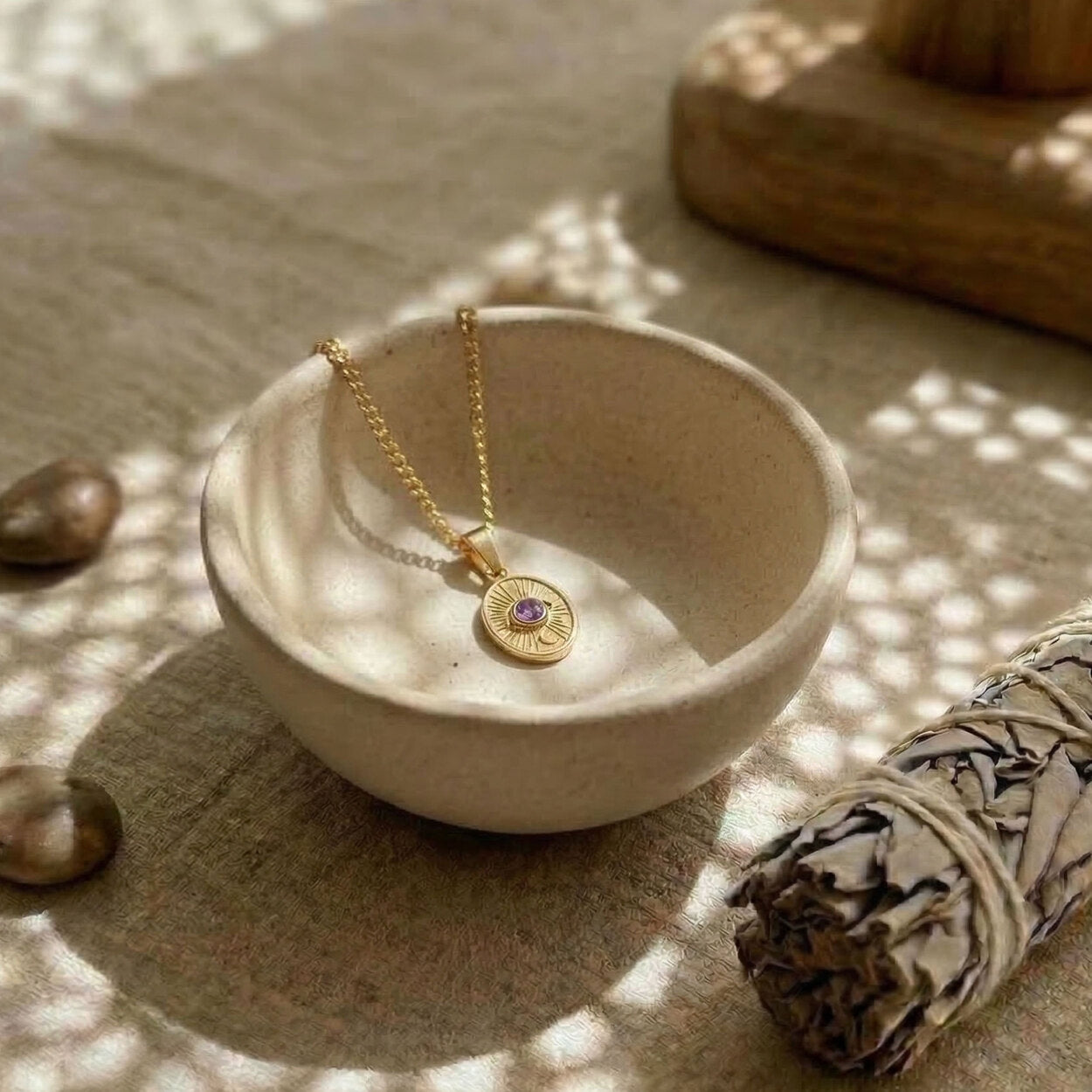 Close-up of the Divine Eye pendant in 14K gold featuring a brilliant-cut purple sapphire and organic hand-finished edges.