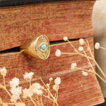 Divine Eye gold ring with turquoise stone displayed on a book with dried flowers – symbolic protection jewelry by Sages & Souls