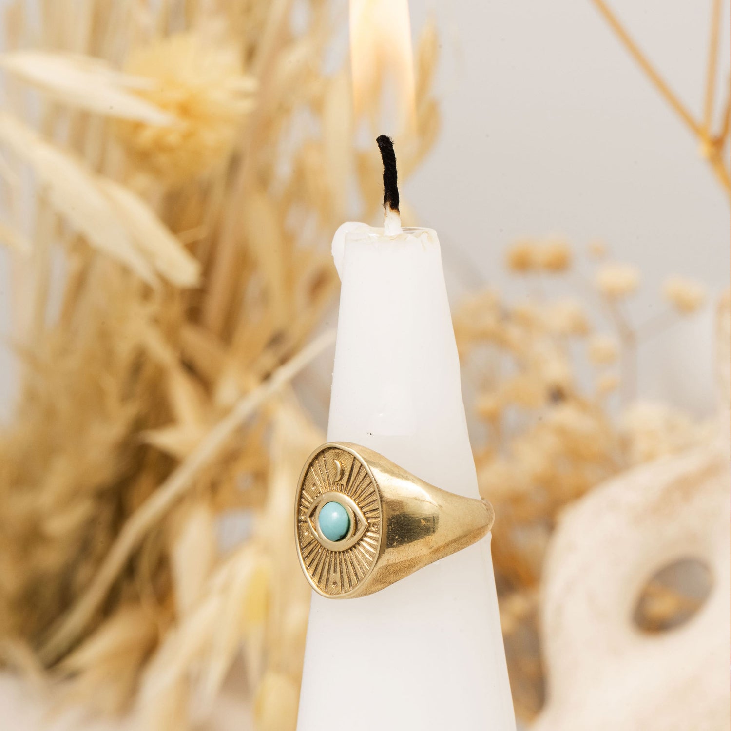 Divine Eye ring resting on white candle with dried floral background – spiritual turquoise gold ring by Sages & Souls