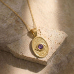 Detail view of the Wisdom and Sefirot pendant in 14K gold with a natural faceted purple sapphire on a textured stone background.
