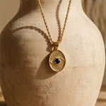 Detailed view of the Protective Eye pendant showcasing the radiating gold lines and secure bezel-set dark blue sapphire.