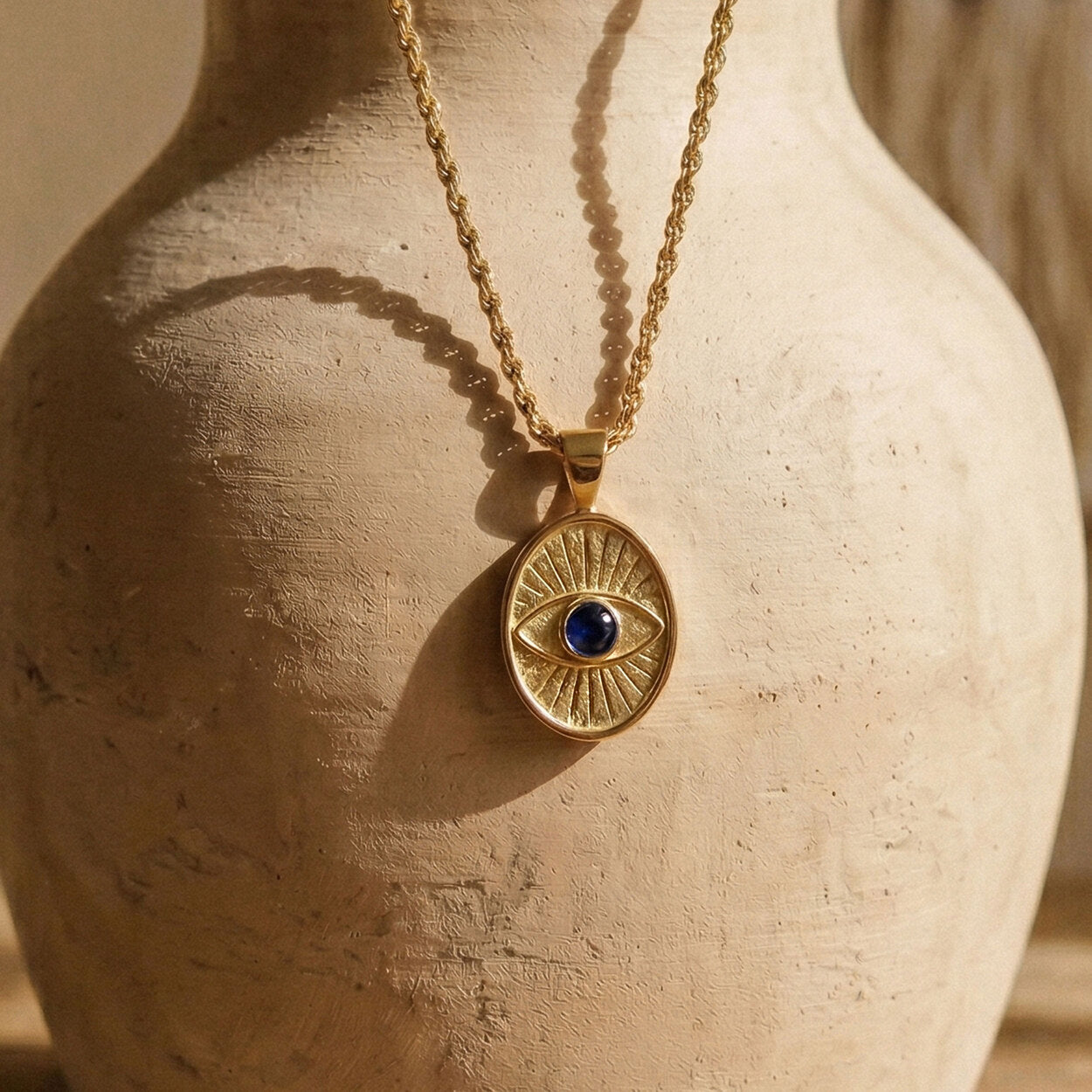 Detailed view of the Protective Eye pendant showcasing the radiating gold lines and secure bezel-set dark blue sapphire.