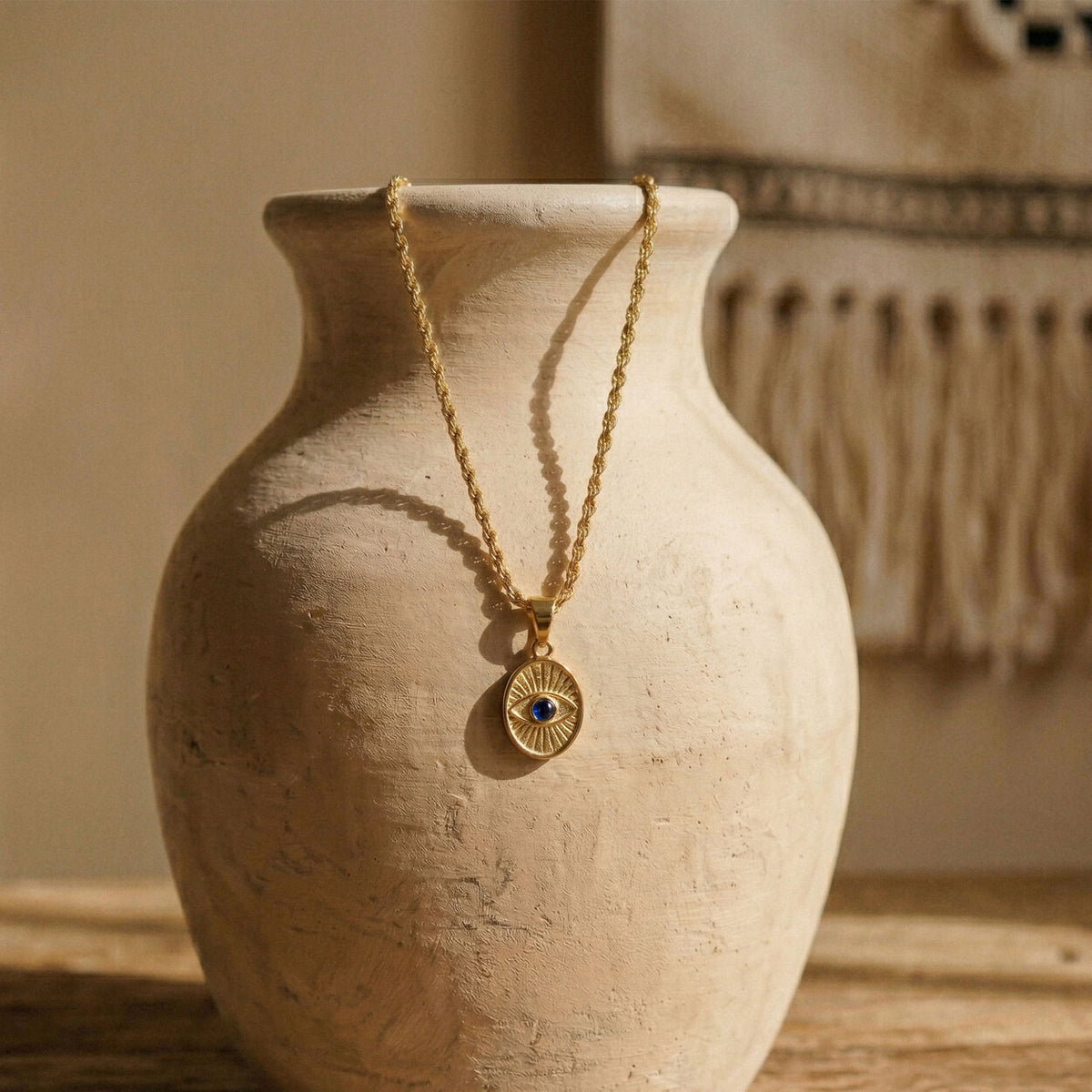 The Protective Eye necklace draped over a ceramic vessel, highlighting the substantial 4.47 gram solid gold weight and sacred eye design.