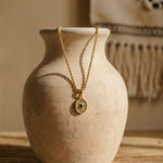 The Protective Eye necklace draped over a ceramic vessel, highlighting the substantial 4.47 gram solid gold weight and sacred eye design.
