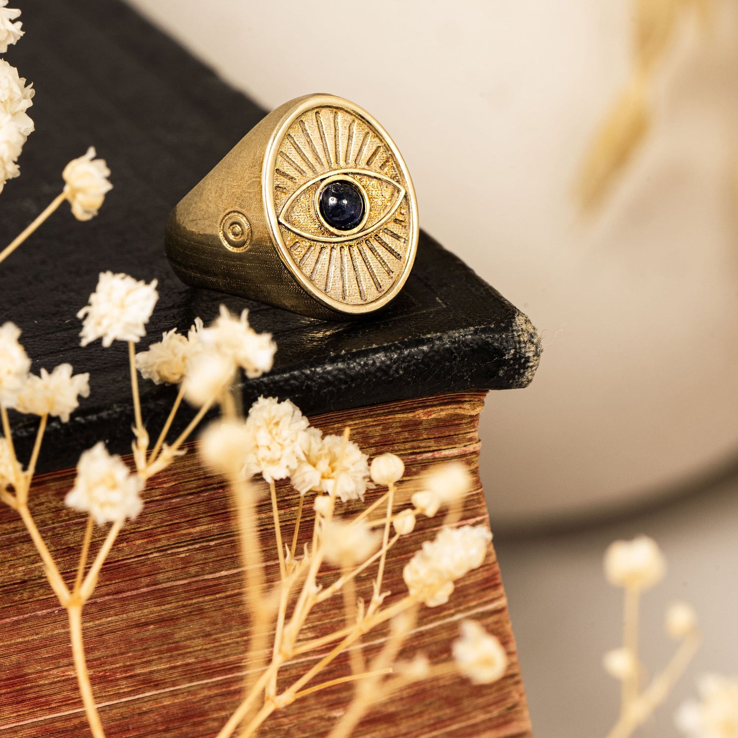 Protective Eye Ring displayed on black book cover beside dried florals
