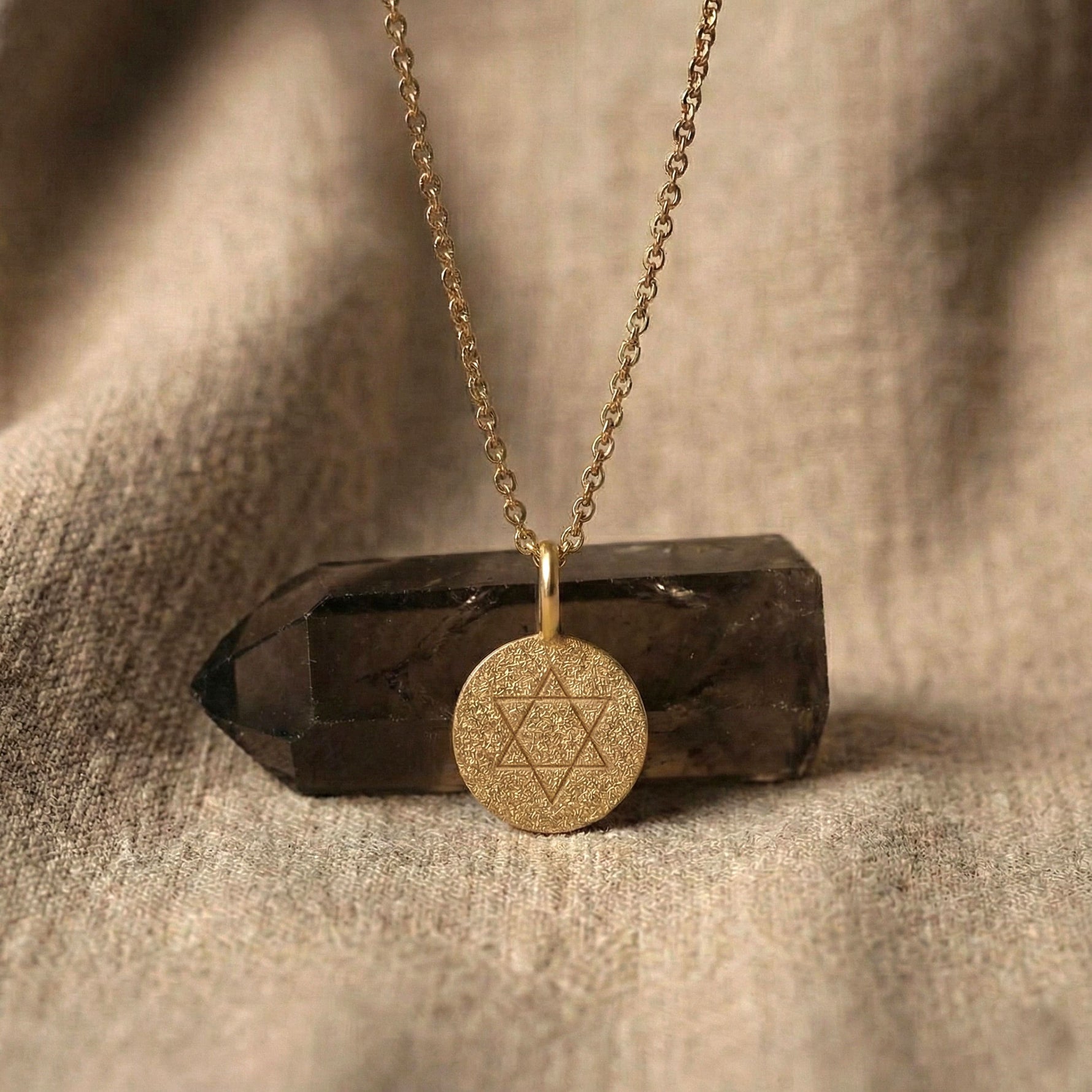 Classic Star of David coin necklace in 18K gold vermeil displayed on a crystal stone over soft fabric.