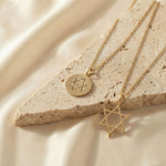 Gold Star of David and Classic Coin necklaces from Sages & Souls styled on a natural stone slab with soft satin background.