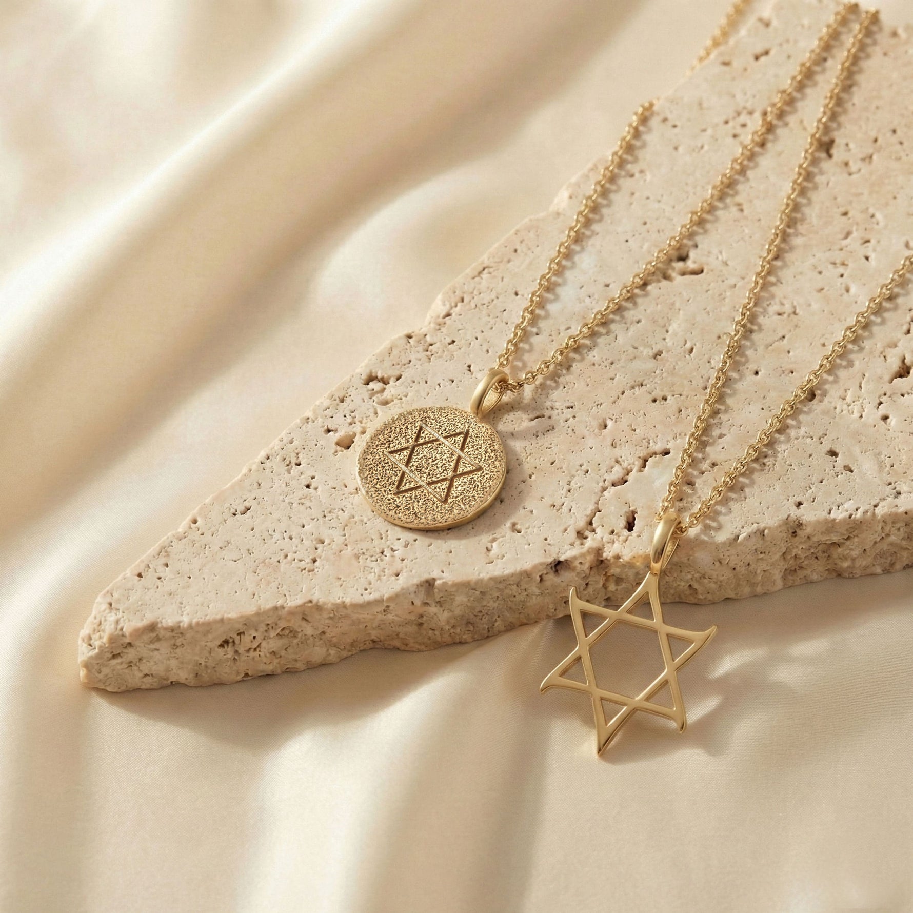 Gold Star of David and Classic Coin necklaces from Sages & Souls styled on a natural stone slab with soft satin background.