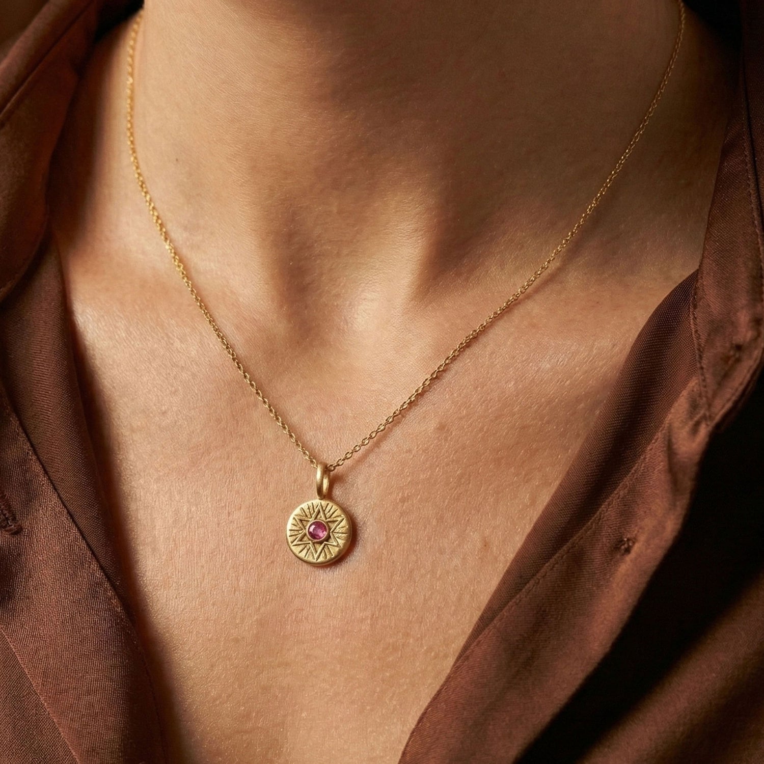 Woman wearing the Radiant Star of David necklace in 18K gold vermeil with a pink sapphire, holding the pendant close.