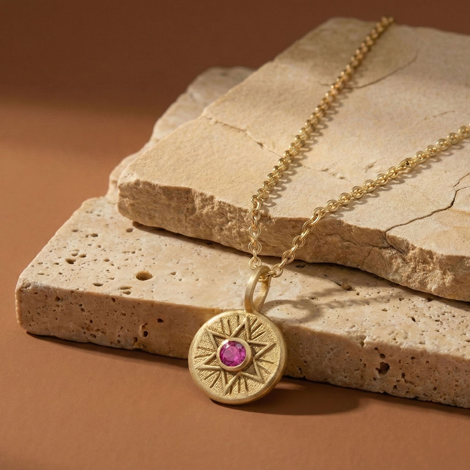 Radiant Star of David necklace in 18K gold vermeil with a pink sapphire, styled on natural stone slabs.