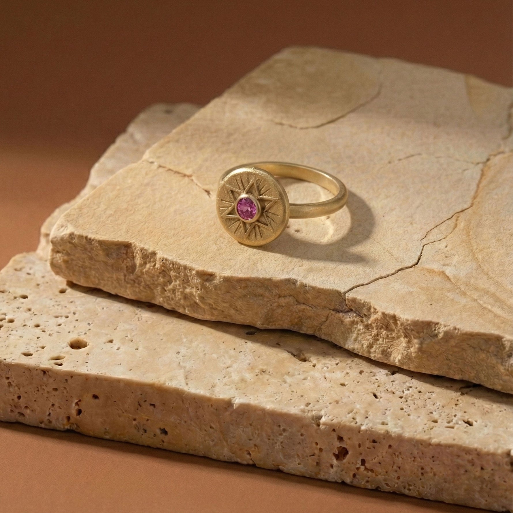 Radiant Star of David ring in 18K gold vermeil with a pink sapphire, displayed on textured stone slabs.