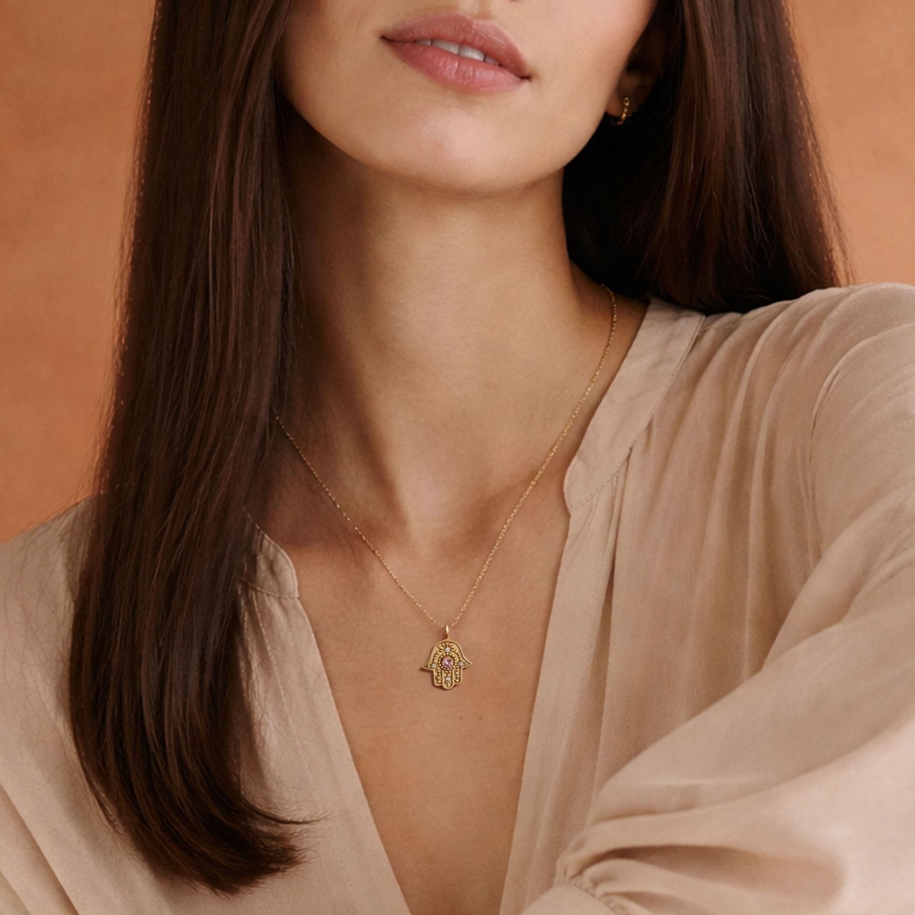 Woman wearing the gold Eternal Pulse Hamsa necklace over a light beige linen blouse.