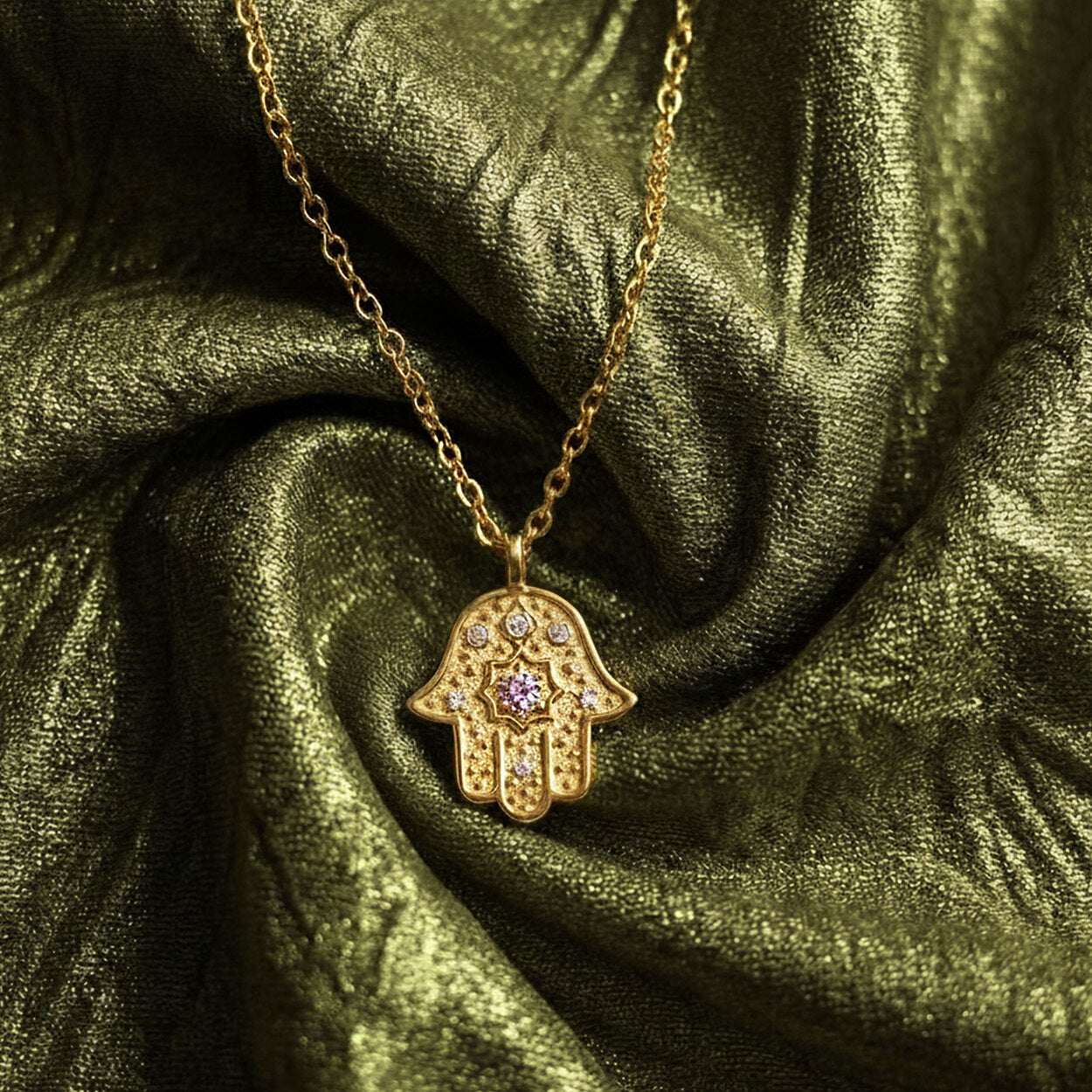 Gold Radiant Anchor Hamsa necklace resting on draped olive green silk fabric.