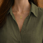 Woman wearing the gold Radiant Anchor Hamsa necklace over an olive green linen shirt.
