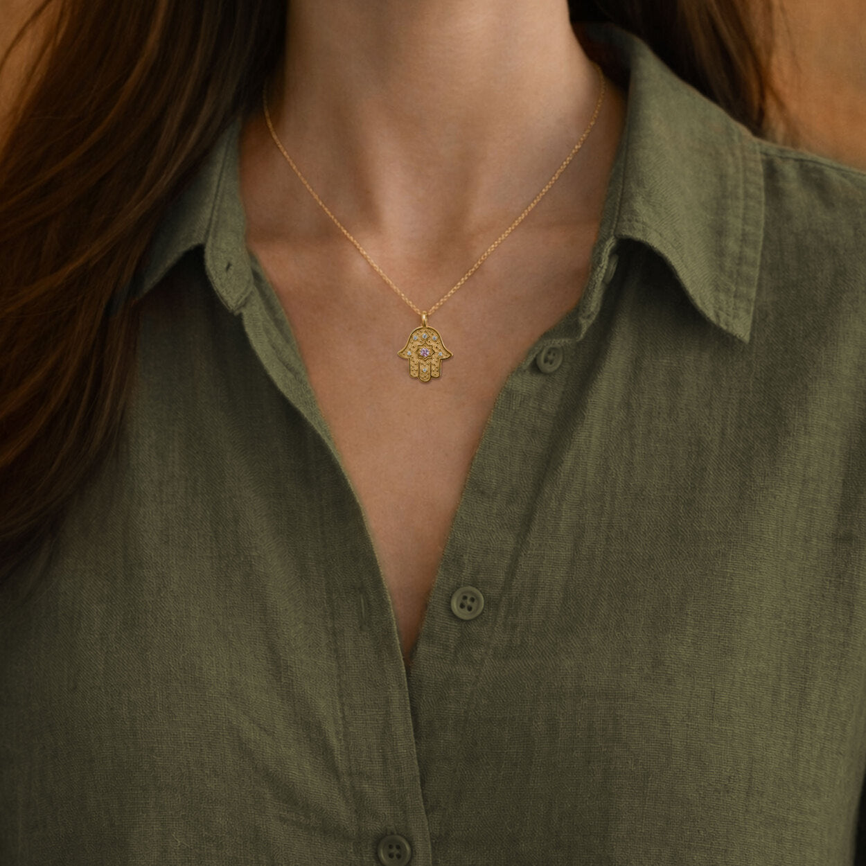 Woman wearing the gold Radiant Anchor Hamsa necklace over an olive green linen shirt.