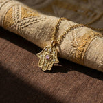Close-up of gold Radiant Anchor Hamsa on a woven rustic fabric.