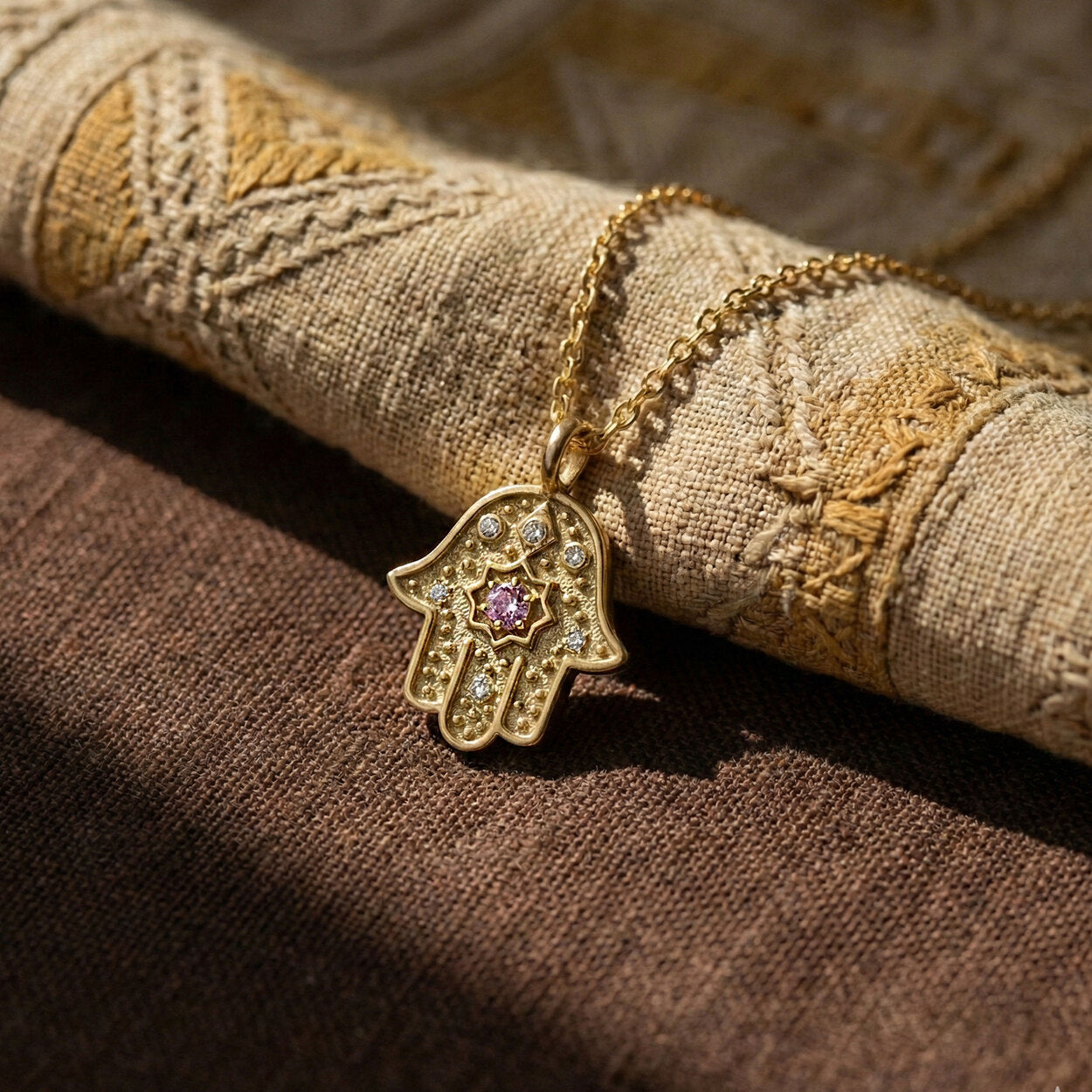 Close-up of gold Radiant Anchor Hamsa on a woven rustic fabric.