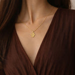 Gold Vine of Lineage Hamsa necklace with pink sapphire worn over a dark brown dress.