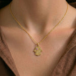 Gold Vine of Lineage Hamsa necklace with pink sapphire worn over a dark brown dress.