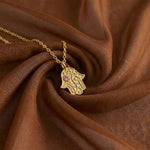 Gold Vine of Lineage Hamsa necklace resting on swirled brown silk fabric.
