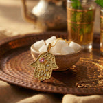 Gold Hamsa necklace leaning against a sugar bowl on a copper tray with mint tea.